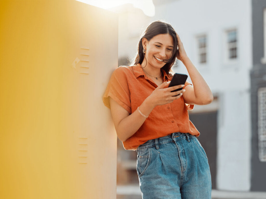 Female looking at phone while leaning against a wall.